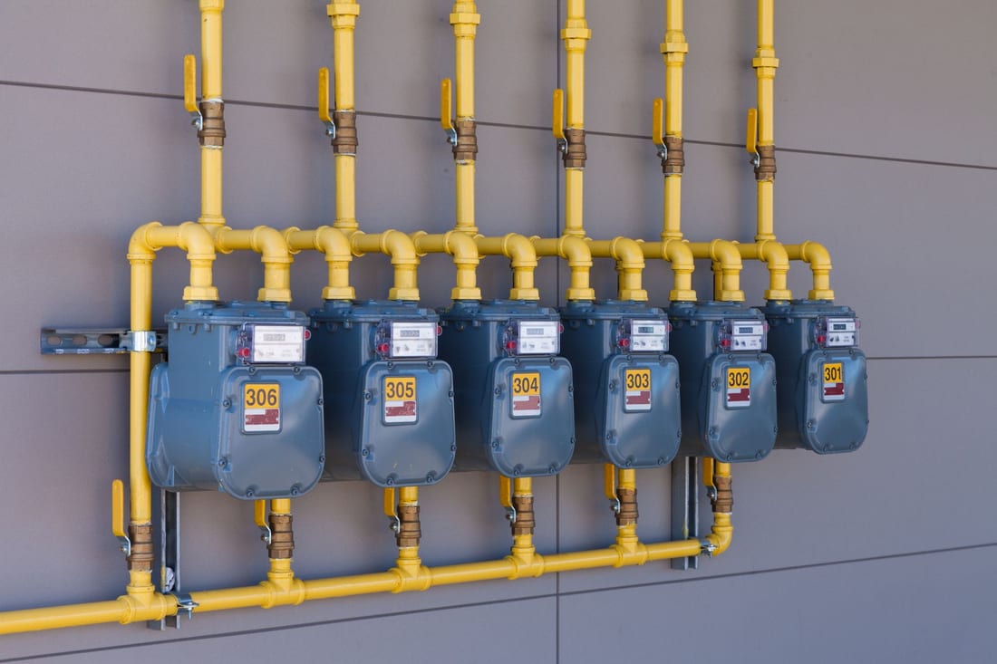 Row of gas meters connected with yellow gas piping on a wall