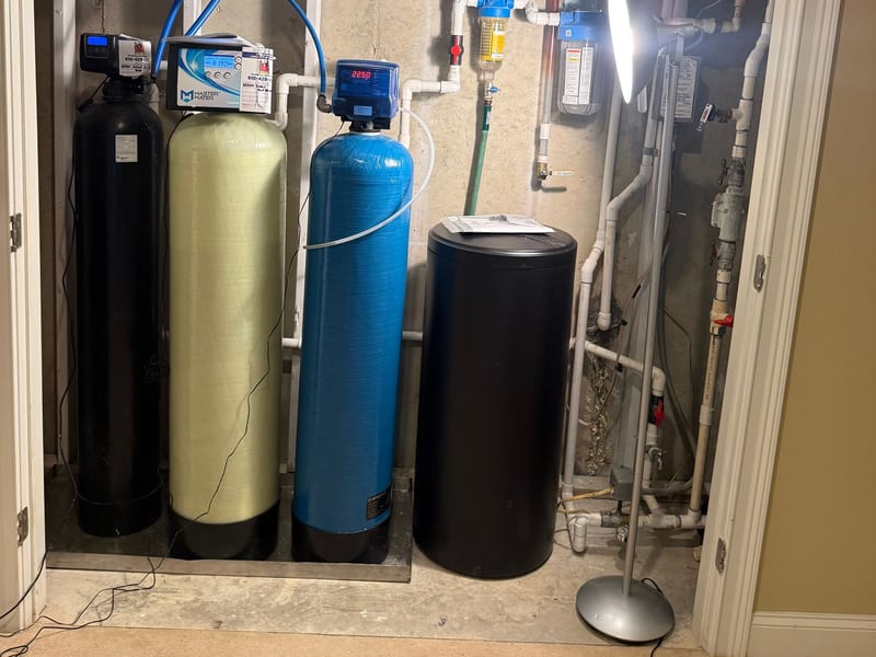 Bank of water treatment tanks, a blue pressure tank and a control head in a basement doorway