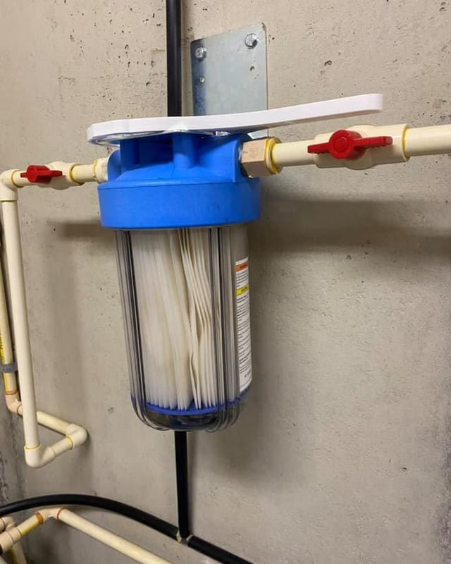 Whole house sediment filter in a blue housing with red shutoff valves on a concrete wall