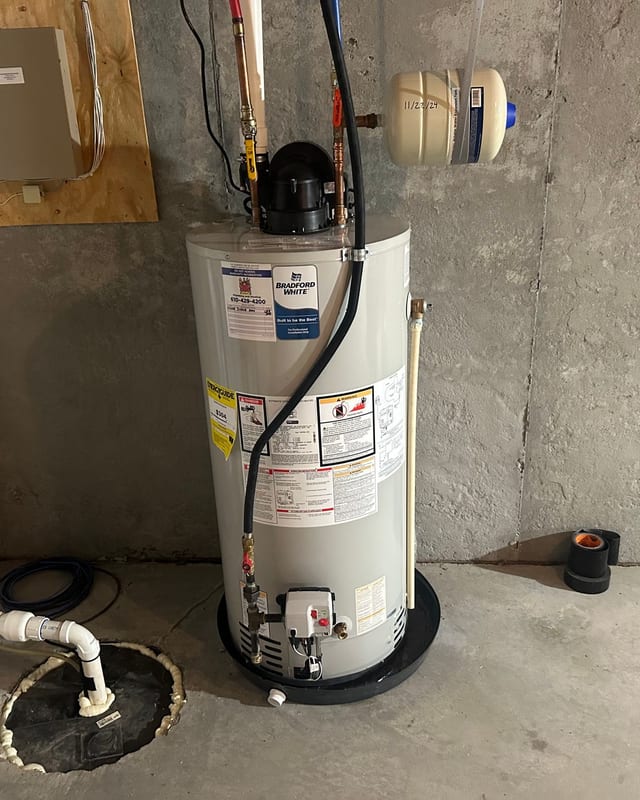 Gas water heater beside a sump pit with white drain piping